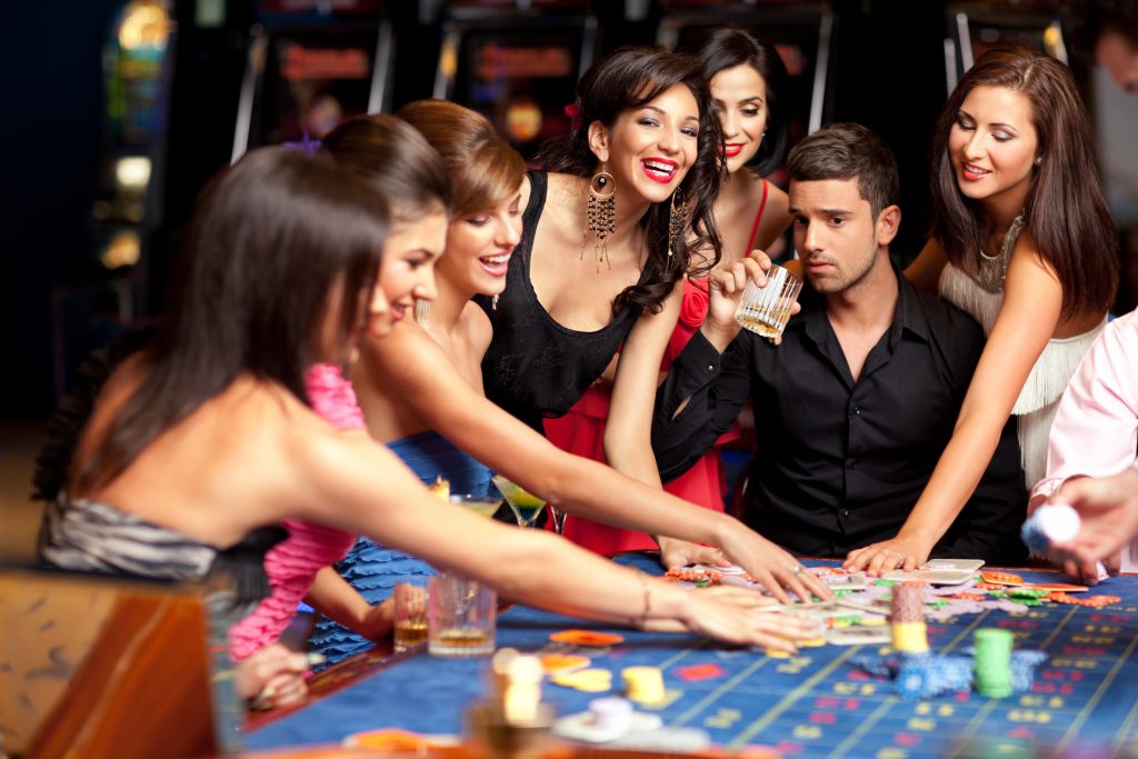 A woman picking a ball from the Roulette wheel with players in the background
