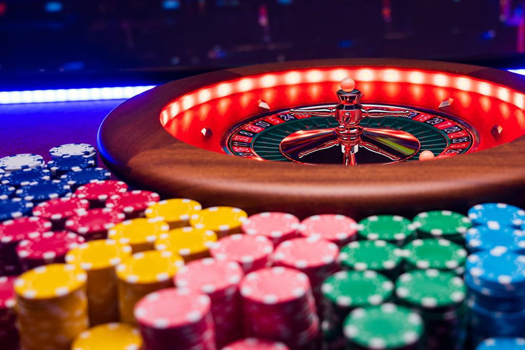 Multi-Colored Betting Chips Stacked Next to a Roulette Wheel
